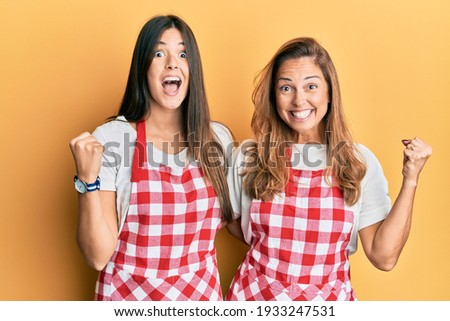 Hispanic family of mother and daughter wearing baker uniform over yellow background screaming proud, celebrating victory and success very excited with raised arms 
