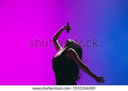 Portrait of young female singer isolated on blue-pink background. Royalty-Free Stock Photo #1933266080