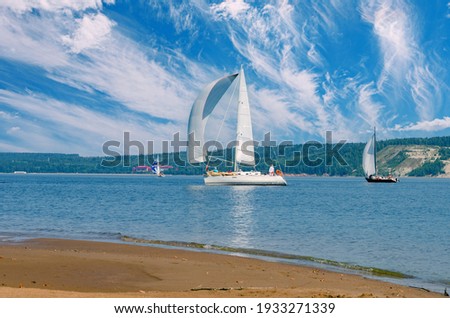 Sailing yachts sail under a beautiful blue sky with cirrus clouds, the reflection of the sun in the water.