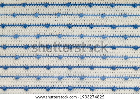 Crochet product from multicolored threads. Handmade backdrop. Flat lay. Fragment of a plaid of blue and ivory tone. Striped, geometric pattern. Royalty-Free Stock Photo #1933274825