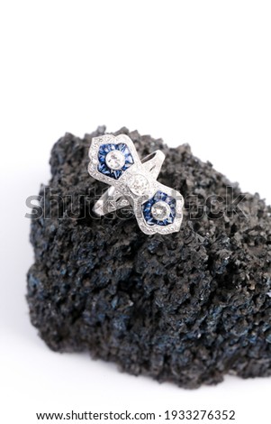 An art deco style sapphire and diamond ring on a dark black rock with a white background