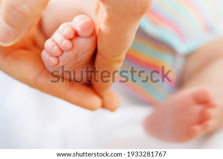 Father or mother holding foot of newborn baby. Adult hand and baby tiny baby feet. Happy parenthood, carefree childhood, family, love, tenderness.