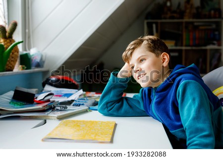 Hard-working happy school kid boy making homework during quarantine time from corona pandemic disease. Healthy child writing with pen, staying at home. Homeschooling distance learning concept.