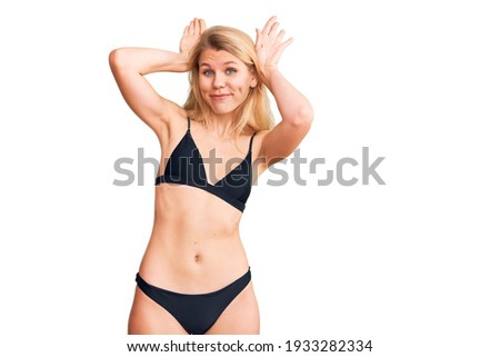 Young beautiful blonde woman wearing bikini doing bunny ears gesture with hands palms looking cynical and skeptical. easter rabbit concept. 