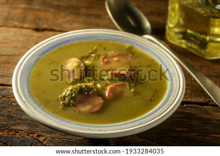 green broth with pepperoni and cabbage top view on rustic wooden table with selective focus glass of oil and pepper grinder
