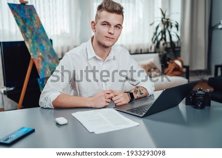 Portrait of a young man in office and his professional occupation as a photographer. Male photographer in comfortable office in daytime.