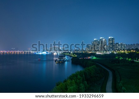 It is a beautiful night view of the city. It's a nice picture, including a river and a promenade through which the boat passes.