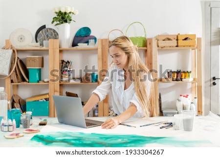 Creative artist watching a sketch of a painting on a laptop while sitting in an art studio