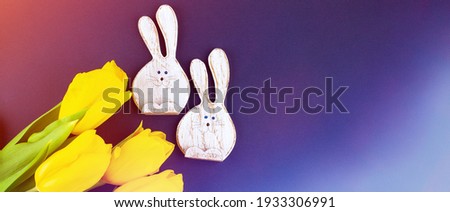 Two Funny Wooden Rabbits and Yellow Tulips on color Background. Concept - Easter Banner with Copy Space for Text. Flatlay. Close up.