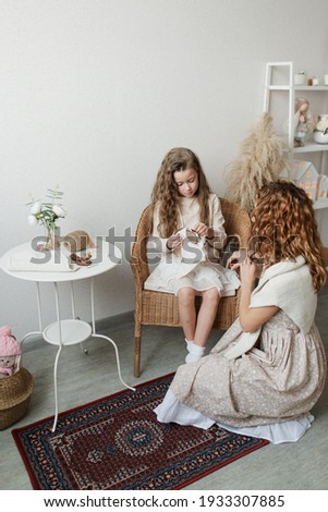 a little girl with her mother embroider on a fabric in a bright room