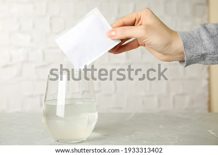 Woman pouring powder from medicine sachet into glass of water on grey marble table, closeup