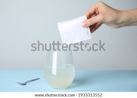 Woman pouring powder from medicine sachet into glass of water on turquoise table, closeup