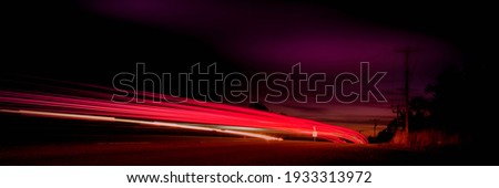 Red Car Light Trails on Highway. Speed Motion Night Background. Curving Light Traveling into Darkness. Panoramic Horizontal close-up with Black Space for Text or Design.
