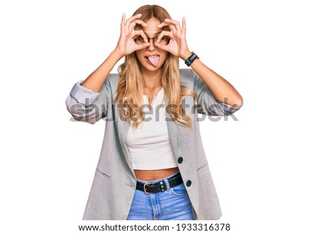 Beautiful blonde young woman wearing business clothes doing ok gesture like binoculars sticking tongue out, eyes looking through fingers. crazy expression. 