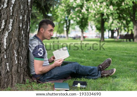 Student with skateboard and backpack reading in the grass