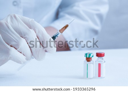 The doctor holds a syringe for the injection of insulin in his hand. There are ampoules of medicine or vaccination on the table in front of the doctor. Vaccination against Covid. Two-component vaccine