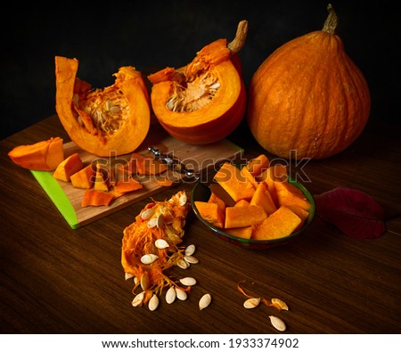 Bright still life with cut orange pumpkins and pumpkin seeds on dark background.Shallow depth of field.