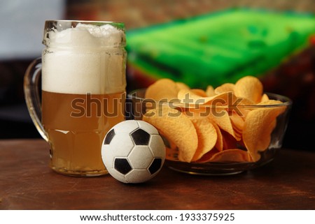 Beer glass, soccer ball and chips in front of screen. Football fans concept