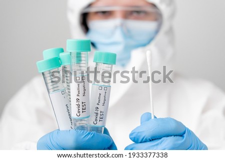 Doctor in PPE suit and face mask demonstrates test tubes with coronavirus Covid-19 samples. Royalty-Free Stock Photo #1933377338