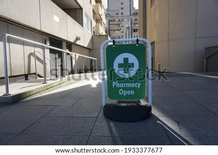 Green and white sign shows Pharmacy Open at the front of alleyway to pharmacy shop