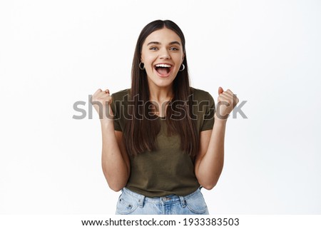 Image of happy young woman winning prize, making fist pump and smiling excited, triumphing as achieve goal, celebrating victory, shouting amazed, white background Royalty-Free Stock Photo #1933383503