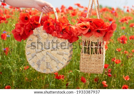 Two wicker handbags with red poppies in a woman's hand against the background of a poppy field. Summer landscape. The concept of happiness, peace, love of life.