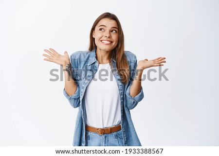 Silly me. Cute smiling woman acting clueless, shrugging shoulders and looking away as if know nothing, have no idea, standing unaware against white background Royalty-Free Stock Photo #1933388567