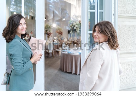 Wedding planners, organizers, event decorators, florists. Young beautiful women, girls in stylish suits at entrance to restaurant. Business meeting, negotiations,signing contract with client,customer. Royalty-Free Stock Photo #1933399064