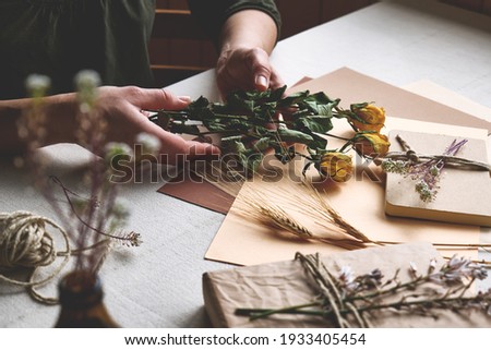 Woman makes zero waste, plastic free, trendy hand made gift card with craft recycled paper and dried flowers on the table with linen tablecloth. Natural aestetic.