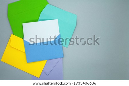 Multicolored envelopes on a gray background. One blue envelope with a blank white card. Mockup with envelope and blank card. Space for text.
