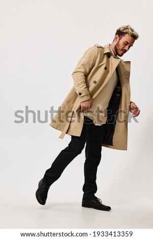 a man in a beige coat, trousers and a sweater bent over to the side on a light background in full growth. High quality photo