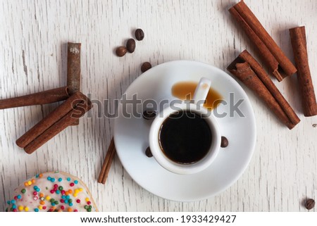 A cup of aromatic black coffee. Spilled coffee. Grains of coffee on the table. Morning espresso or Americano coffee for breakfast in a beautiful cup. Still life. Cinnamon sticks. Wooden background.