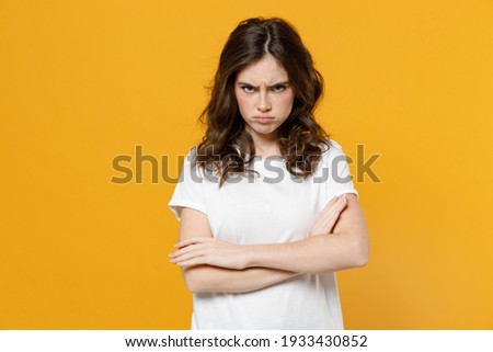 Young offended angry indignant frowning caucasian student woman 20s in white basic casual t-shirt look camera holding hands crossed folded isolated on yellow orange color background studio portrait