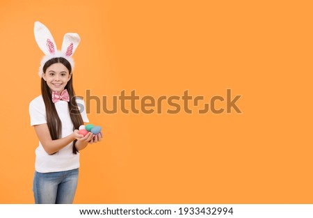 happy easter kid girl in bunny ears and bow tie hold painted eggs, copy space, easter.