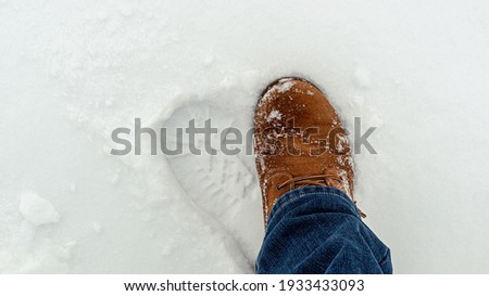 Feet in a suede boot and jeans in the snow. Footprint in the snow