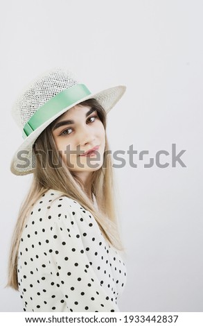 girl in a sundress and straw hat posing on a light, solid background