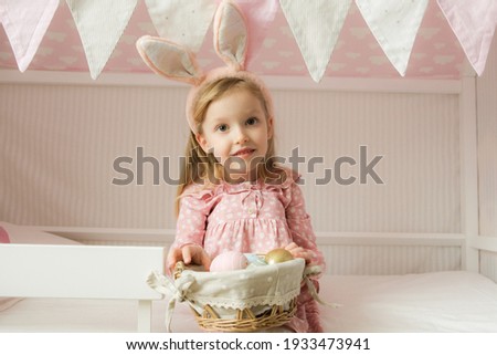 Little girl wearing bunny ears and holding a basket of Easter eggs. Happy Easter. Preparing family for Easter. Easter bunny ears.Smiling face