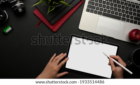 Top view of female hands working on digital tablet with stylus pen on dark creative workspace, clipping path