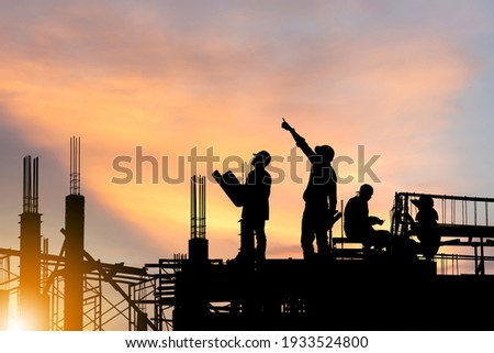 Silhouette of Engineer and worker on building site, construction site at sunset in evening time. Royalty-Free Stock Photo #1933524800
