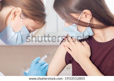Mass global vaccination of teenagers against covid-19 coronavirus, a doctor injects a vaccine to a patient girl Royalty-Free Stock Photo #1933552805
