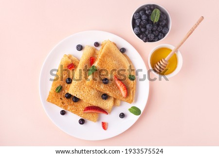 breakfast with russian pancakes with berries and honey on pink background, top view Royalty-Free Stock Photo #1933575524