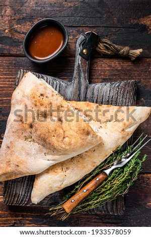 Homemade Calzone closed pizza with ham and cheese on wooden board. Dark wooden background. Top view.