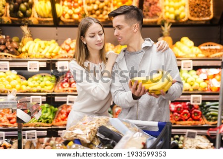 Young positive male and female customers choosing fruits in grocery