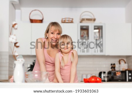 Mom and daughter cook in the kitchen. A young woman cooks with her child in the kitchen at home. Girls in pink clothes cook pizza. Happy and cheerful mom and daughter

