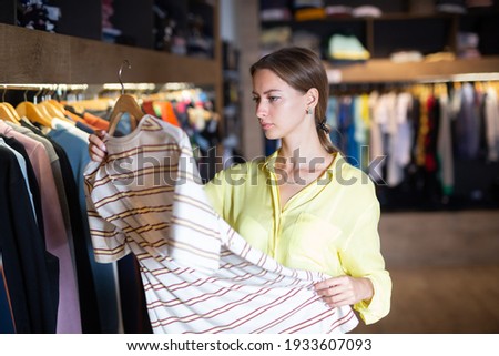 Young female shopper looking for men clothing on rack with hangers in store