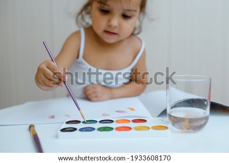 Close up of a little child girl painting with her watercolors with a brush.