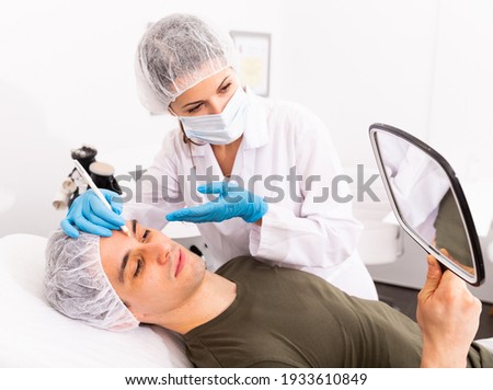 Confident woman cosmetologist examining male client face before procedure in esthetic clinic