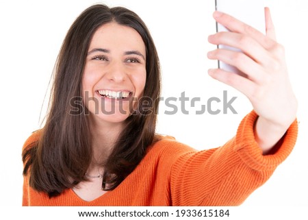 Joyful happy woman holding mobile phone and smiling taking selfie isolated over white background