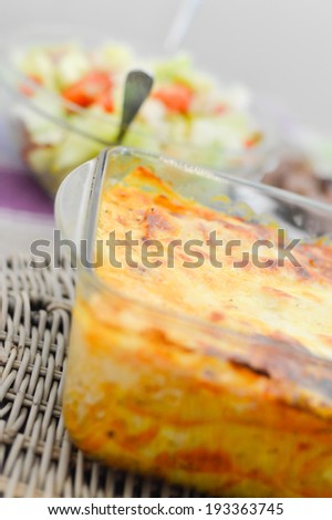 picture of baked homemade lasagna in glass bowl closeup and salad on background 