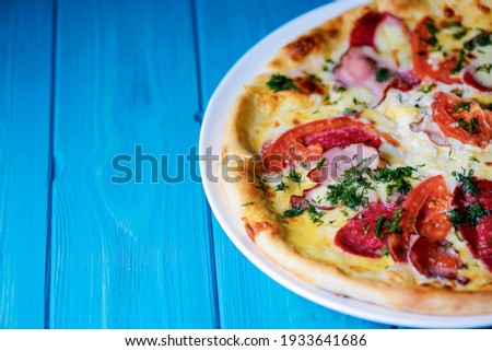 Cooked pizza on aged blue wooden surface background with copy space, side view. Fast food, junk food concept. Italian pizza traditional recipe.